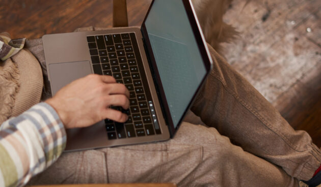 Vertical cropped picture of male hands typing on keyboard, using laptop and petting the dog, cafe visitor working and spending time with his puppy.